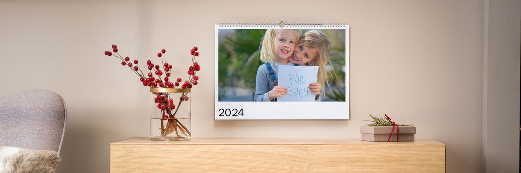 Ein Kalender mit zwei Mädchen auf dem Titelblatt hängt über einer Anrichte in einem Wohnzimmer.