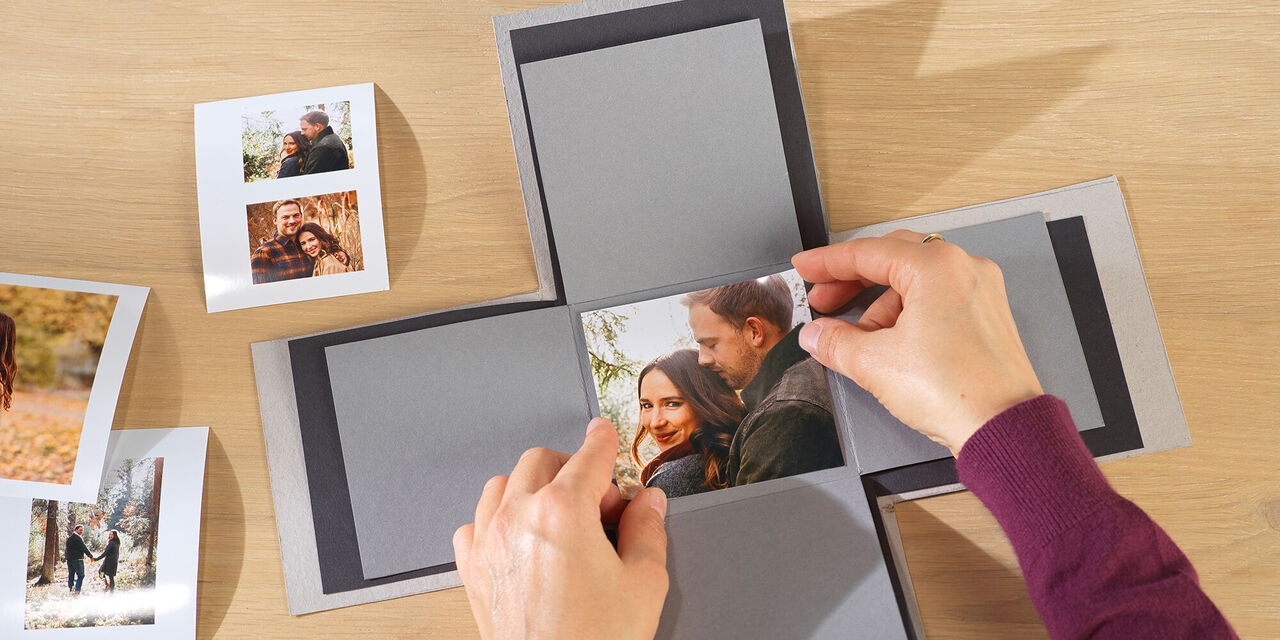 Eine Person platziert ein Foto in eine kreative geschenkte Box mit mehreren Bildern. Diese Gestaltung wird mit viel Liebe durchgeführt und drückt persönliche Gefühle aus.