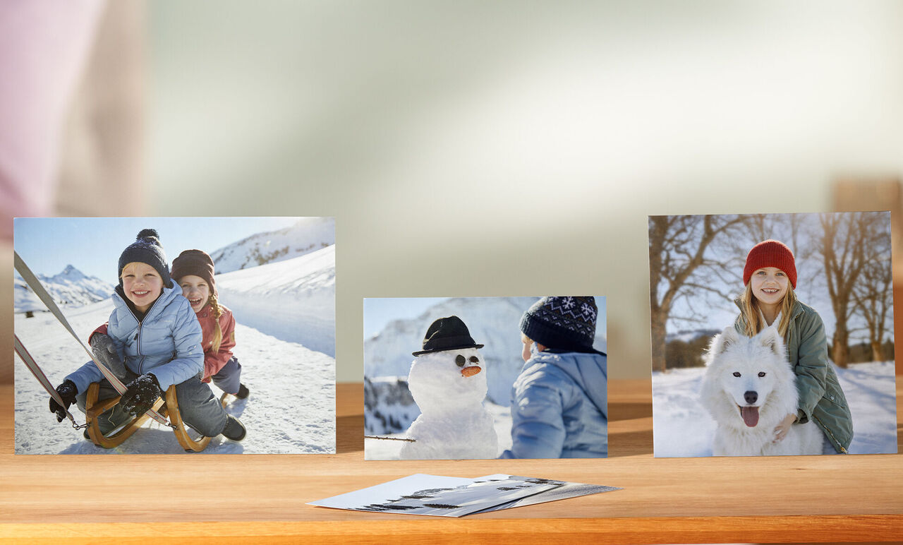 Drei Fotos auf einem Tisch: Kinder im Schnee, ein Schneemann mit Hut und ein Kind mit einem Hund.