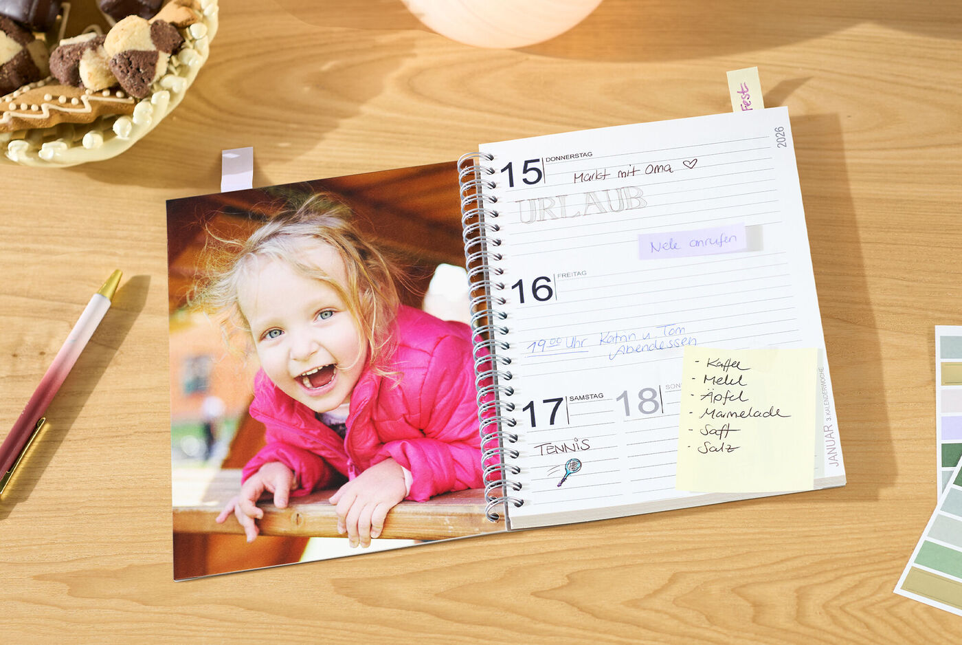 Offener CEWE Fotokalender mit Terminseite und großem Foto eines Kindes in pinker Jacke auf einem Holztisch