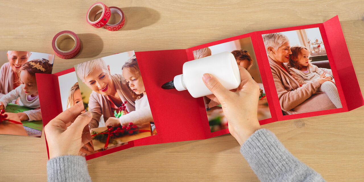 Eine Person gestaltet ein rotes Fotobuch mit schönen Familienfotos
