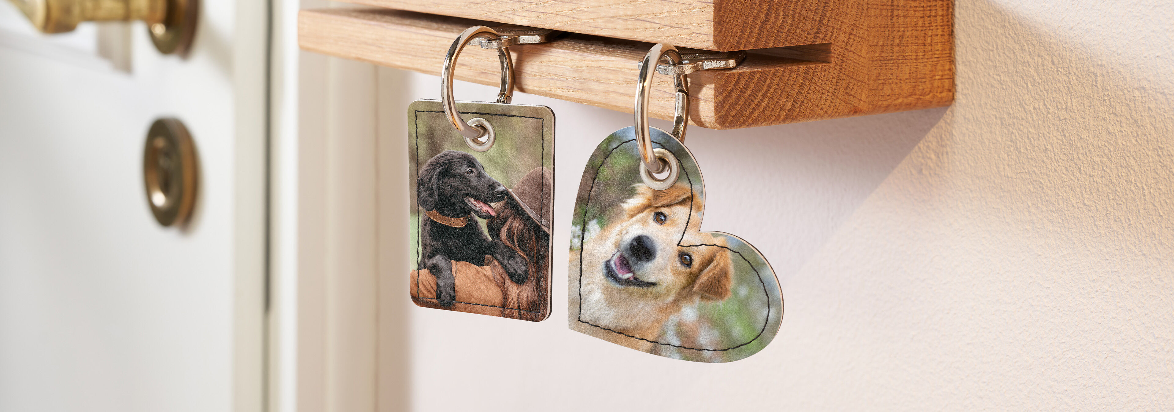 Zwei personalisierte Schlüsselanhänger mit Fotos von Hunden hängen an einem hölzernen Schlüsselbrett.