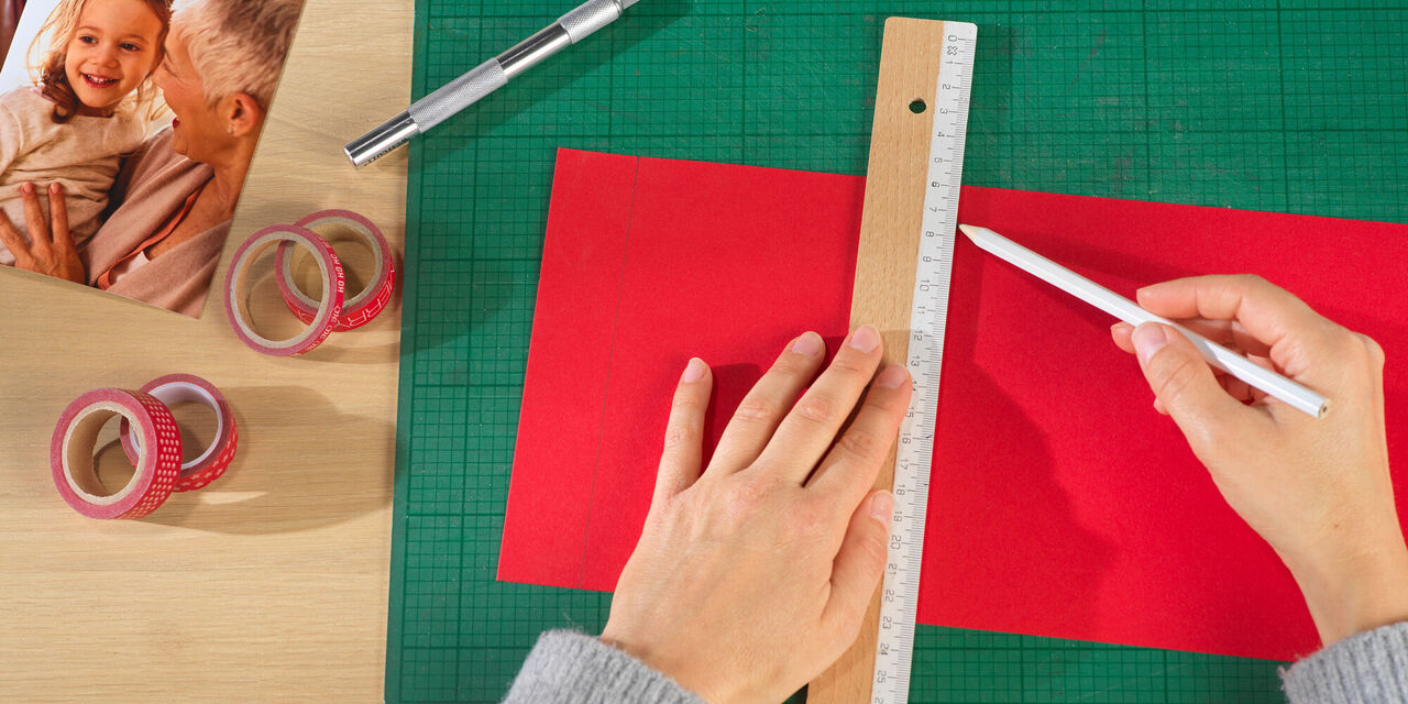 Eine Hand, die auf rotem Papier mit einem Lineal zeichnet, um kreativ zu gestalten