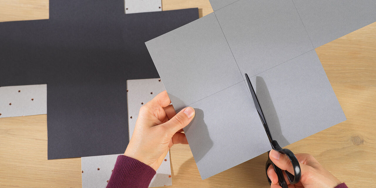 Eine Person schneidet graues Papier mit einer Schere, um eine kreative Geschenkverpackung zu gestalten
