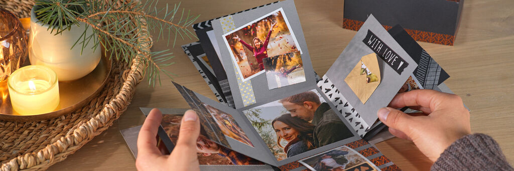 Eine Person blättert durch ein offen liegendes Fotobuch mit glücklichen Erinnerungen und Bildern schöner Momente.