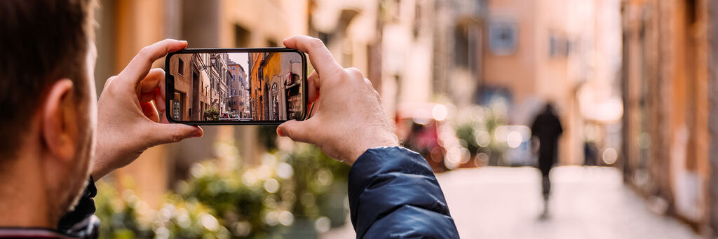 Mann fotografiert eine Straße in Rom mit dem Smartphone.