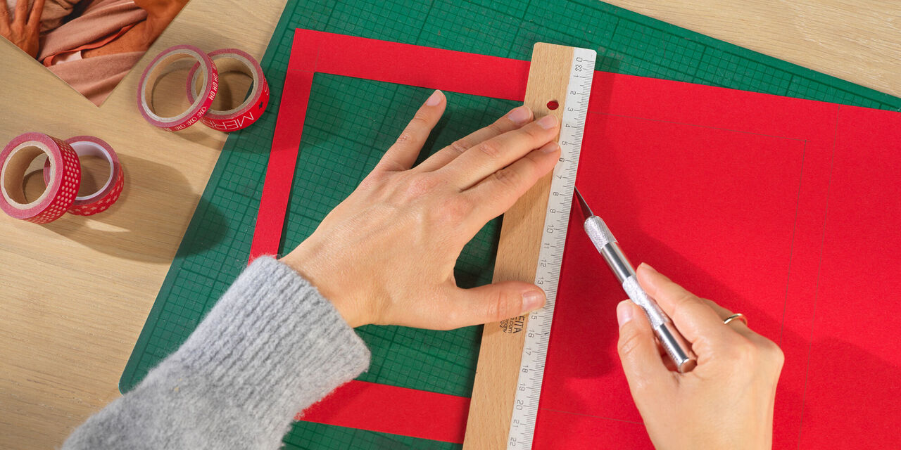 Eine Hand schneidet rotes Papier mit einem Cutter und einem Lineal. Dazu sind Dekobänder und ein weiteres Bild zu sehen.