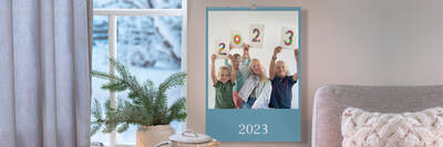 Wandkalender hängt an Wand in Wohnzimmer. Darauf sind vier Familienmitglieder zu sehen, die jeweils ein Schild mit einer Ziffer der Zahl 2021 hochhalten.